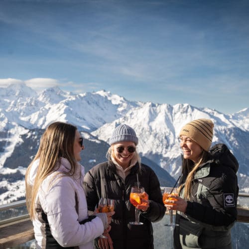3 people drinking Aperol at Apres Ski in front of verbier moutains