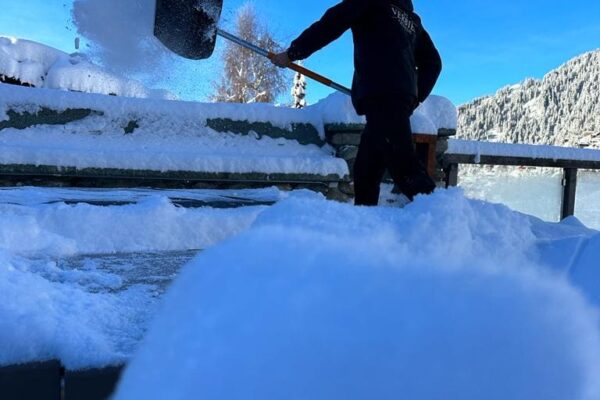 Driver shovelling snow off a snowy chalet terrace in Verbier